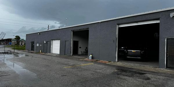 A gray industrial building with open garage doors on a rainy day.