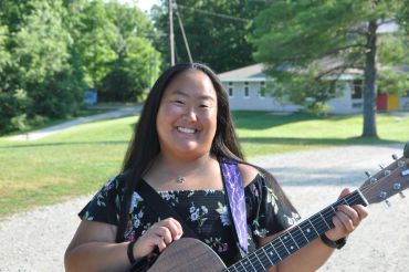 Young woman smiling with guitar outdoors.
