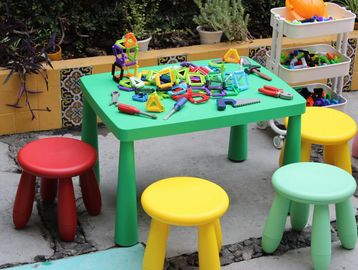 Colorful stools and a green table with scattered magnetic building toys outdoors.