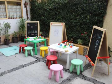 Colorful children's stools and tables with chalkboards set up outdoors for a workshop.