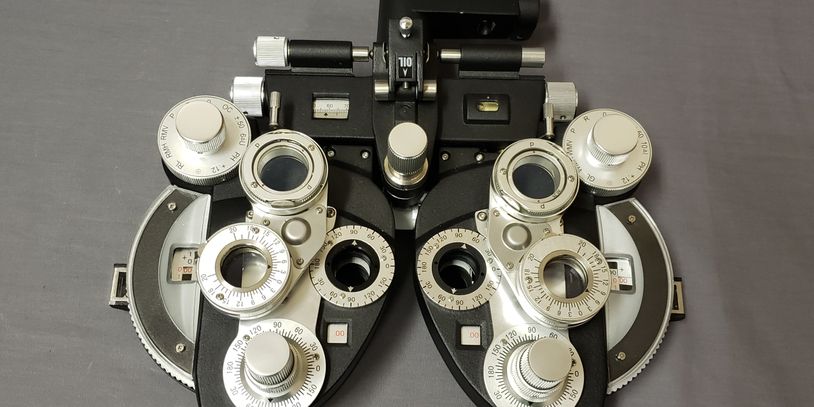 A black and silver optometry device with dials and lenses on a gray surface.