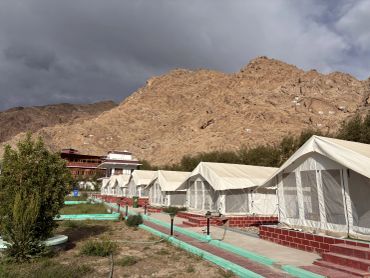 Camp tents with mountainous backdrop under cloudy sky.