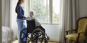 A woman standing by an elder lady on a wheelchair.