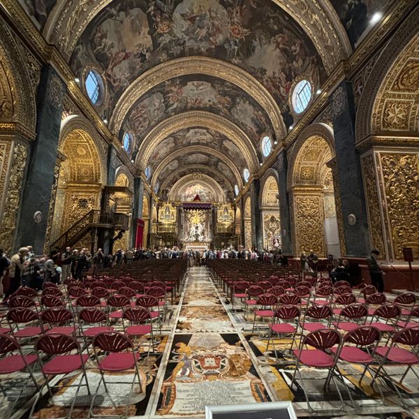 Interior view of an ornate church with painted ceilings and red chairs.