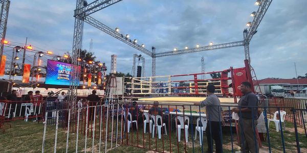 Outdoor boxing ring setup with lighting and audience seating at dusk.
