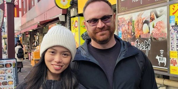A smiling couple posing in front of colorful restaurant signs on a bustling street.