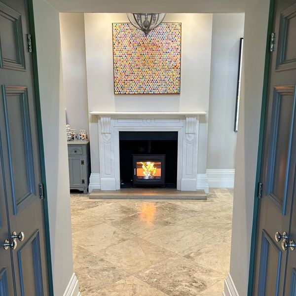 A new log burner installed into a hallway fireplace with beautiful marble floors and stone surround