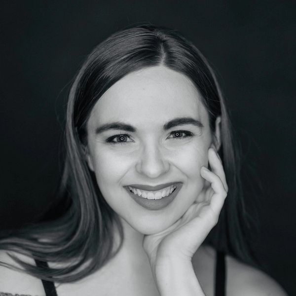 A smiling woman with long hair resting her face on her hand.