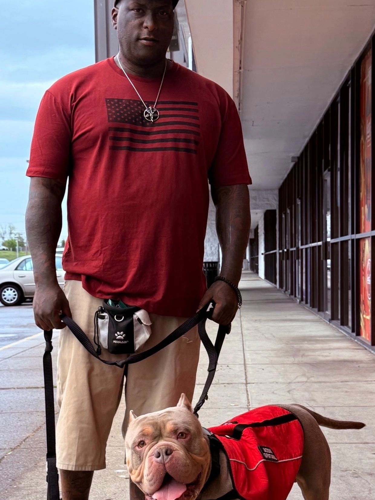 Man in red shirt holding leash of a happy dog wearing a red vest.