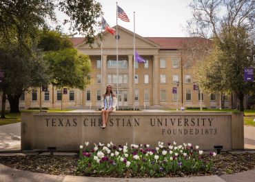 Student sitting in front of Texas Christian University sign.