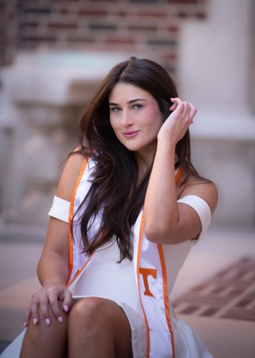 Young woman in white dress with graduation stole.