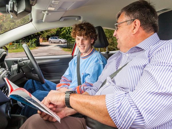 A driving instructor teaches a young student inside a car.