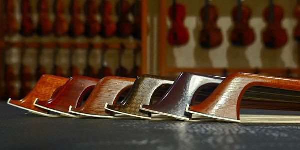 Bows on a table with violins and violas hanging on a rack in the background