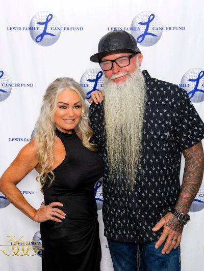 A smiling couple poses at the Lewis Family Cancer Fund event backdrop.
