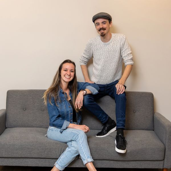 Young man and woman sitting and smiling on a gray couch.