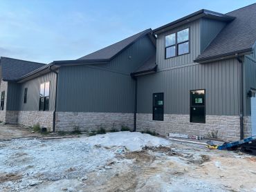 Newly constructed house with gray siding and stone accents under blue sky.
