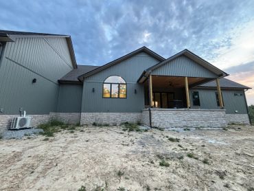 Modern house exterior with gray siding and stone accents under a cloudy sky.