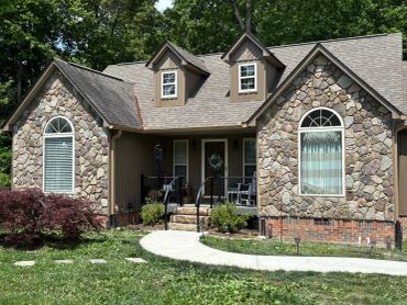 Cozy stone and brick house with a curved walkway and front porch seating.