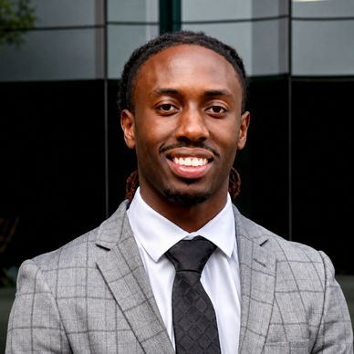A confident man in a gray checkered suit and black tie smiling.