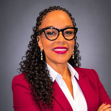 Confident woman in glasses and a burgundy blazer smiles warmly.