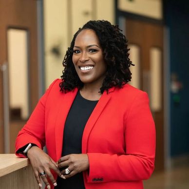 Confident woman in a red blazer smiling indoors.