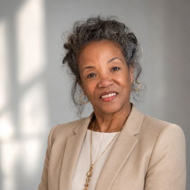 Smiling mature woman in beige blazer with elegant jewelry.