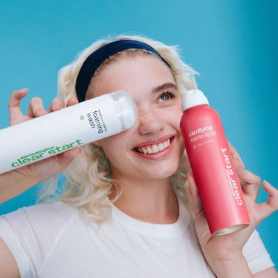 Woman smiling with two skincare products against a blue background.