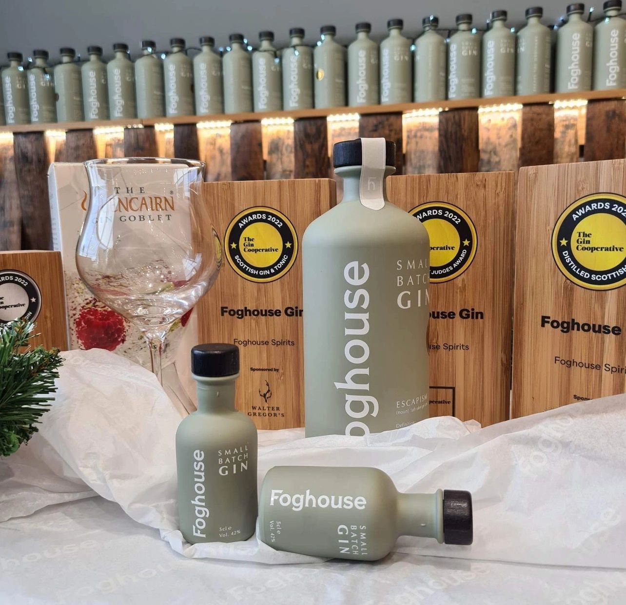 Bottles of Foghouse Small Batch Gin with awards and a gin glass on display.