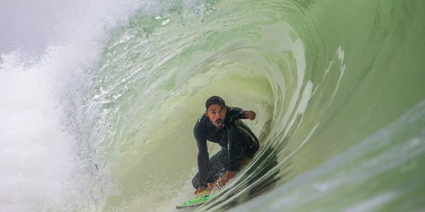 Surfer rides inside a large, green wave tube with focus and skill.