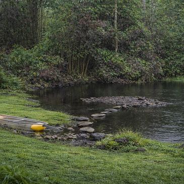 A kayak beside a calm lake surrounded by greenery and stepping stones.