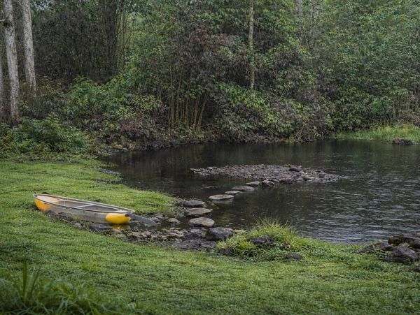 A canoe on the grass near a lake surrounded by trees.