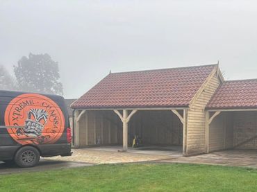 Wooden carport with red tiled roof beside a branded van on a grassy lawn.