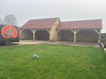 Wooden carport with red tiled roof beside a branded van on a grassy lawn.