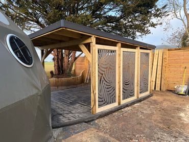 Wooden outdoor shelter with decorative panels and a nearby structure.