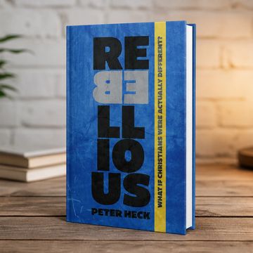 Blue book titled 'Rebellious' by Peter Heck on a wooden table.
