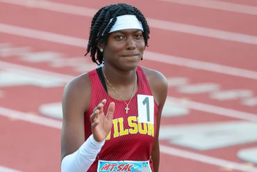 Female athlete in red Wilson uniform on track, waving.