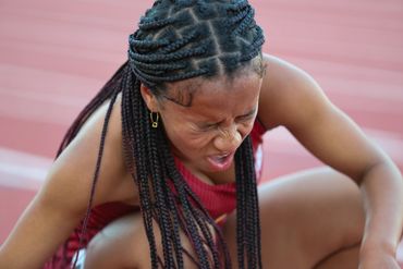 Athlete grimacing in pain, sitting on a track field.