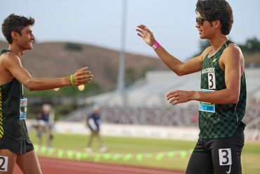 Two male athletes reaching out to each other on a track field.