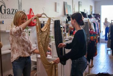 Two women examining a golden dress in a boutique.
