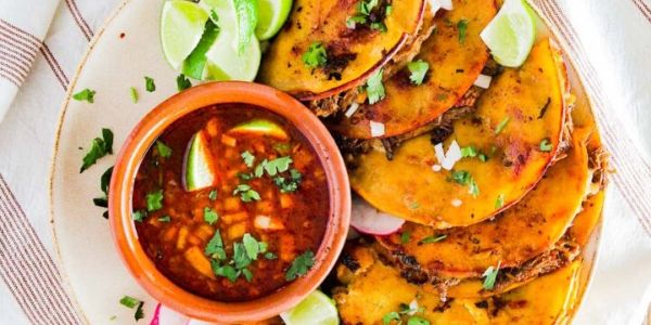 Tacos with salsa and lime wedges on a plate.