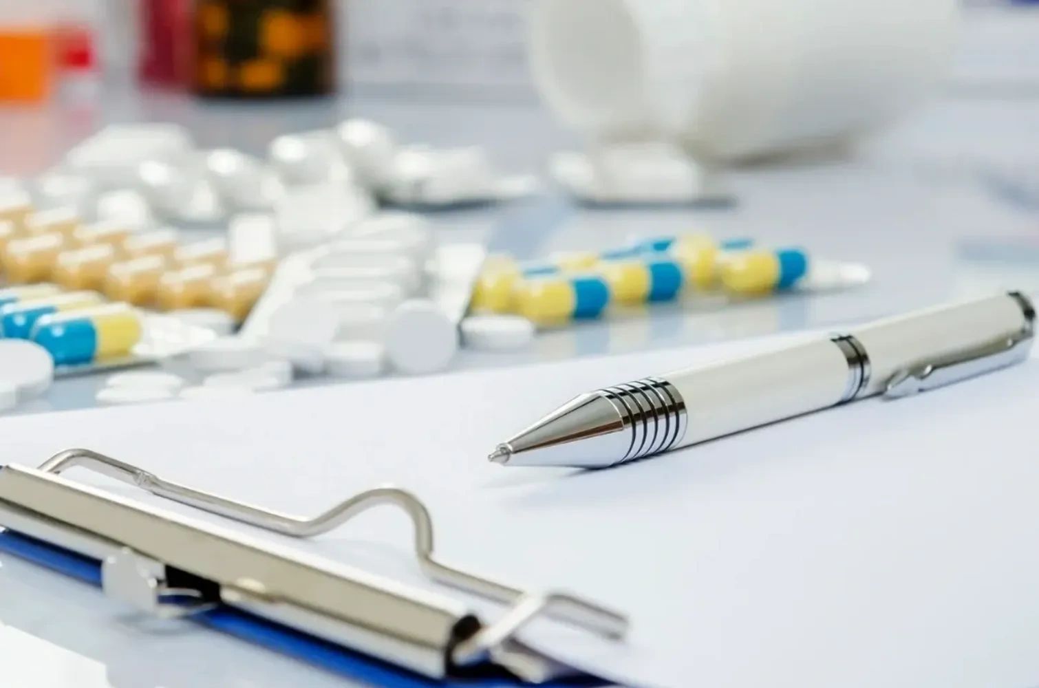 Pen on clipboard with various pills in the background.