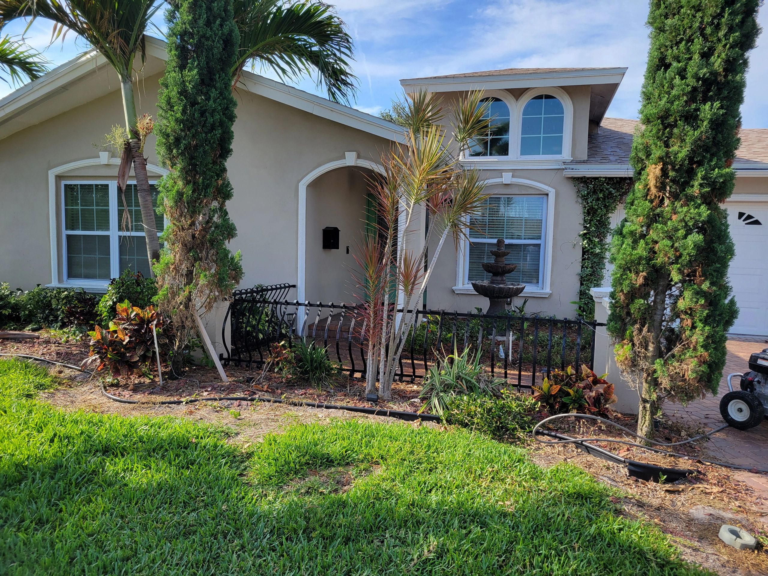 Suburban house with manicured lawn, palm trees, and a decorative water fountain in front yard.