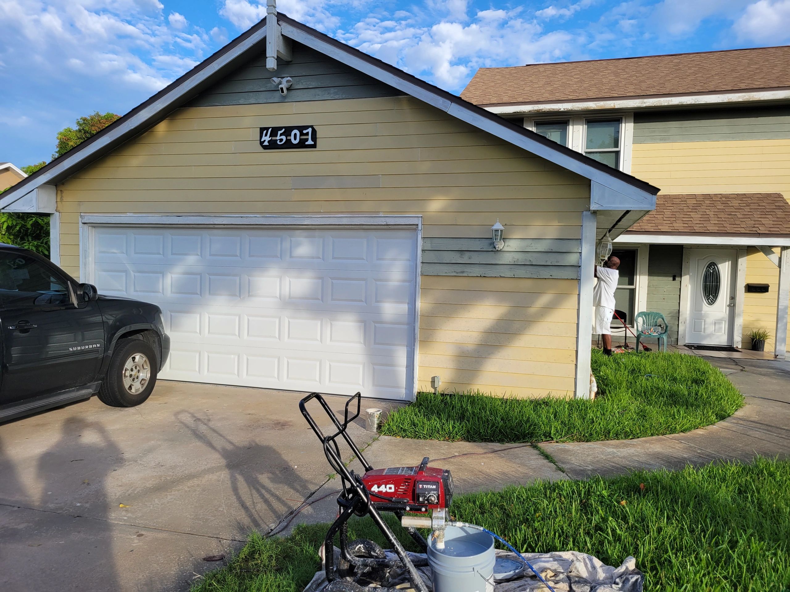 Person painting the exterior of a yellow house with a white garage door.