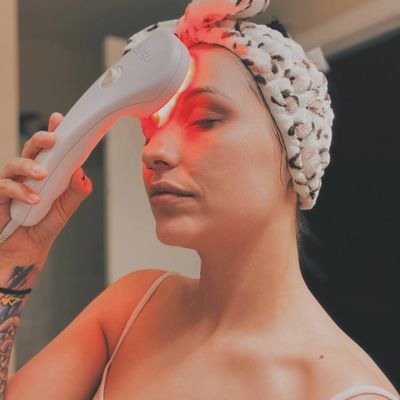 Woman using a red light therapy device on her forehead.
