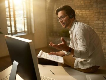 Man with headset engaging in a video call at his desk.