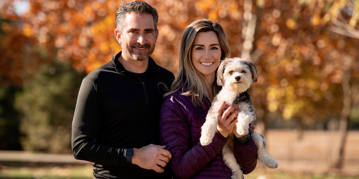 Smiling couple with a small dog outdoors in autumn.