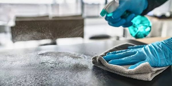A person cleaning a surface with spray and cloth while wearing blue gloves.