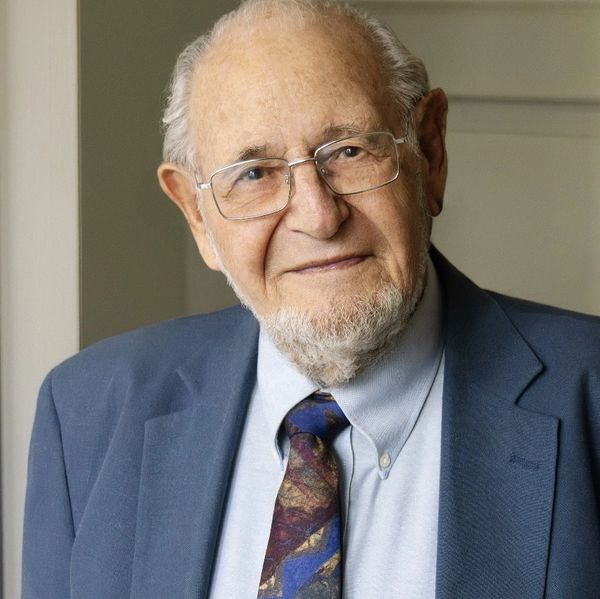 Elderly man in glasses and a suit smiling gently.
