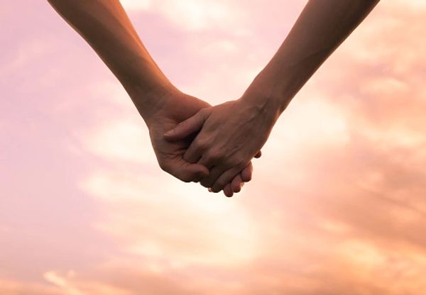 Two people holding hands against a soft sunset sky.
