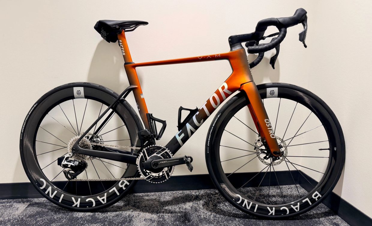 Sleek orange and black Factor road bike against a white wall.